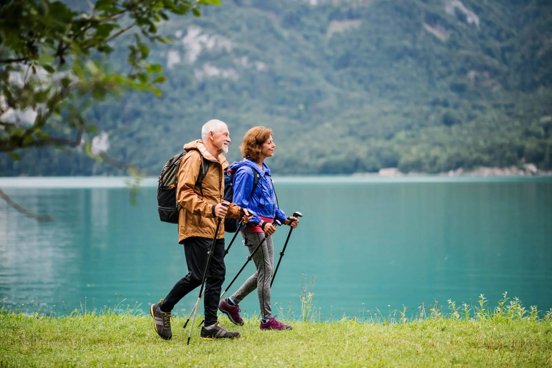 A side view of senior pensioner couple hiking by lake in nature, talking. Copy space.